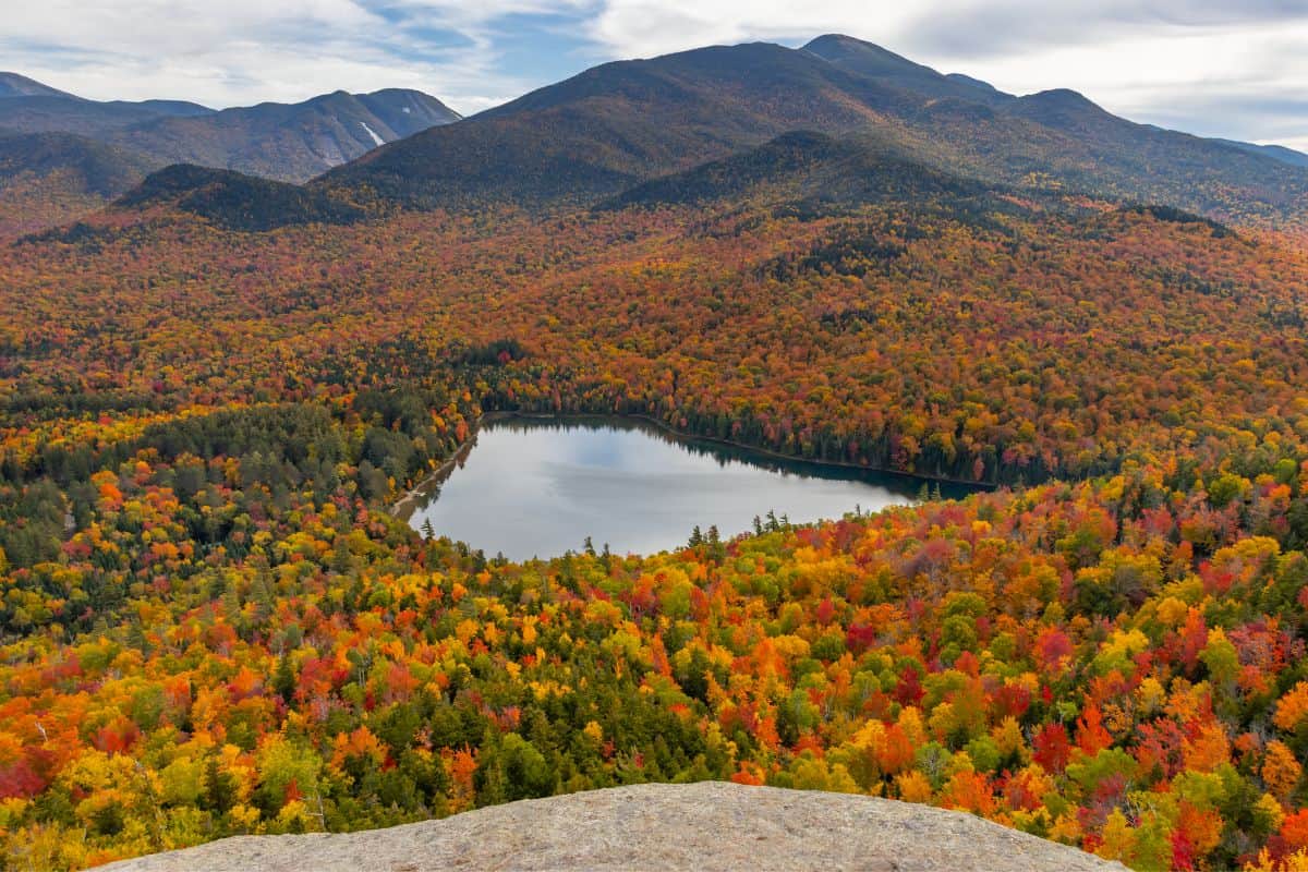 A high-angle view of a mountain lake surrounded by a forest with autumn foliage.