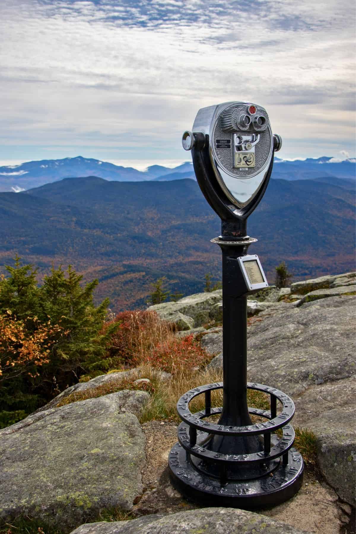 Coin-operated metal viewing binoculars on a mountain summit overlooking a valley.