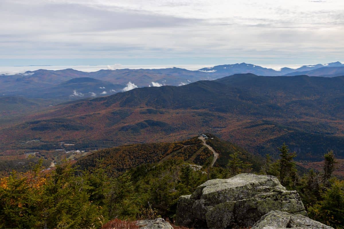 View of a mountainous landscape covered in autumn foliage, with a road leading to a building on a ridge in the distance.