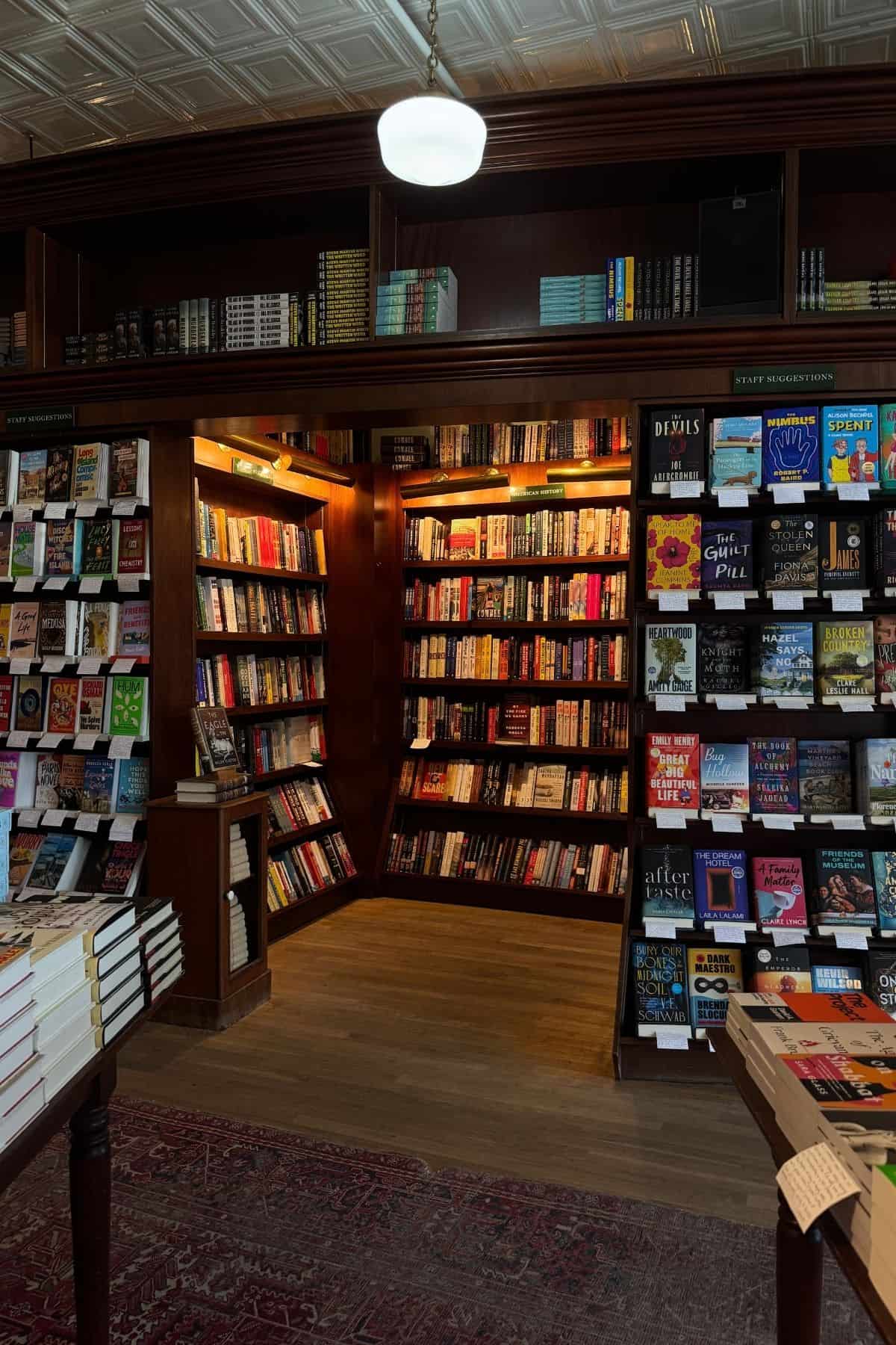 An interior view of a bookstore with floor-to-ceiling wooden shelves filled with books and a “Staff Suggestions” display section.