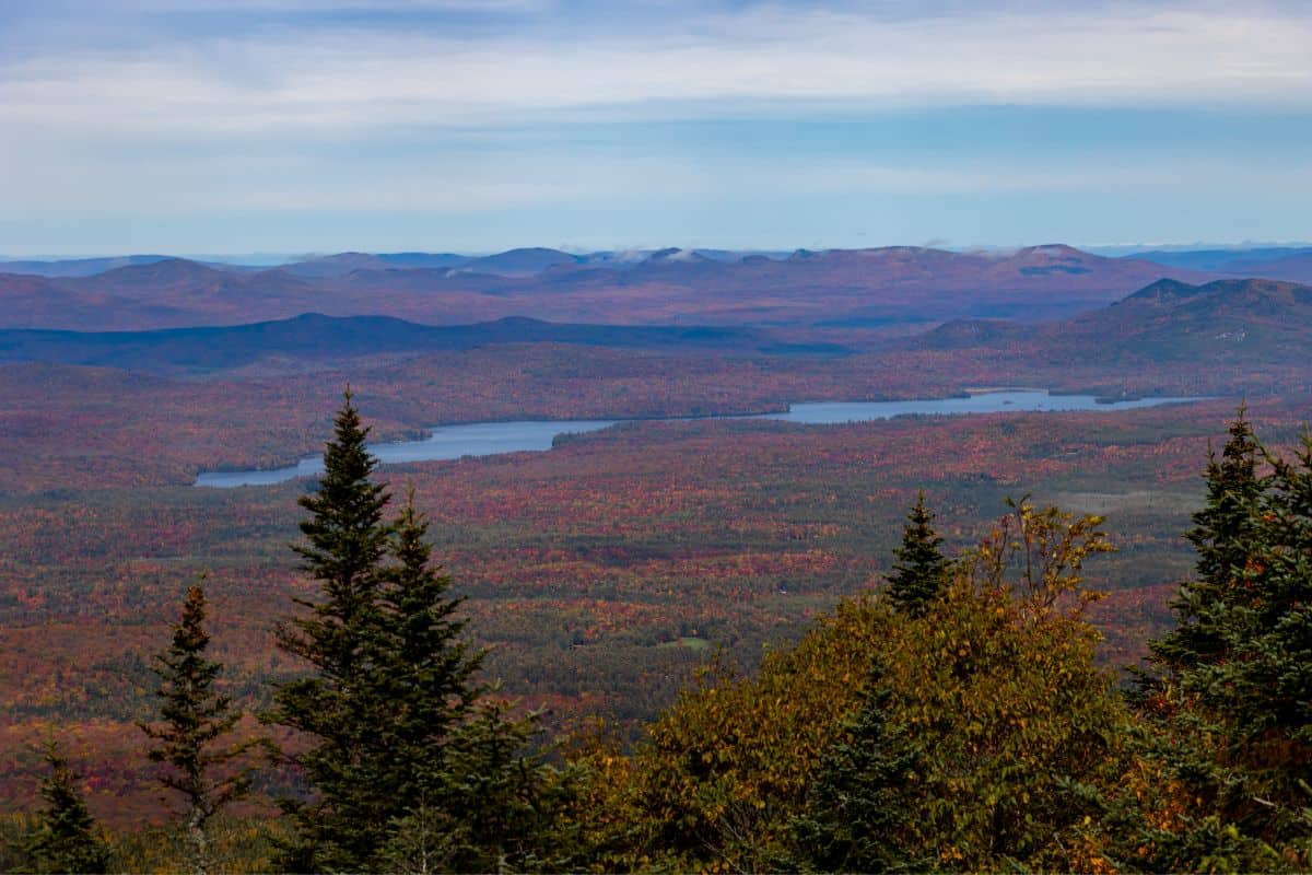A landscape view of a lake surrounded by forest with autumn foliage, seen from a mountain height.