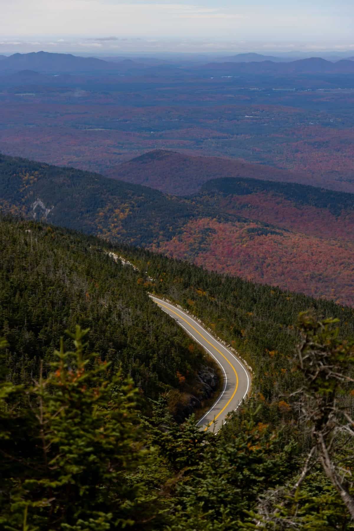 A winding road cutting through a forested mountain landscape with fall foliage.